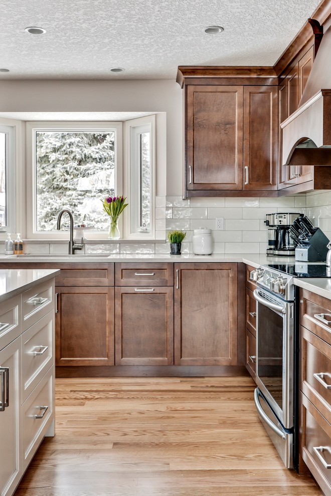 Design ideas for a mid-sized traditional u-shaped eat-in kitchen in Calgary with an undermount sink, shaker cabinets, dark wood cabinets, quartzite benchtops, white splashback, subway tile splashback, stainless steel appliances, light hardwood floors, with island, brown floor and white benchtop.