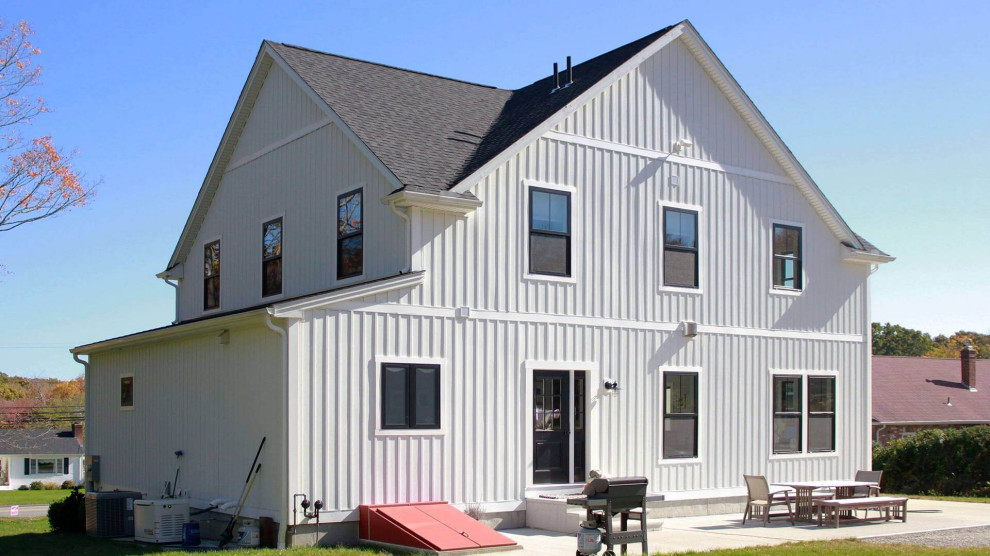 Foto della villa grande bianca country a due piani con rivestimento in vinile, tetto a capanna, copertura a scandole, tetto nero e pannelli e listelle di legno