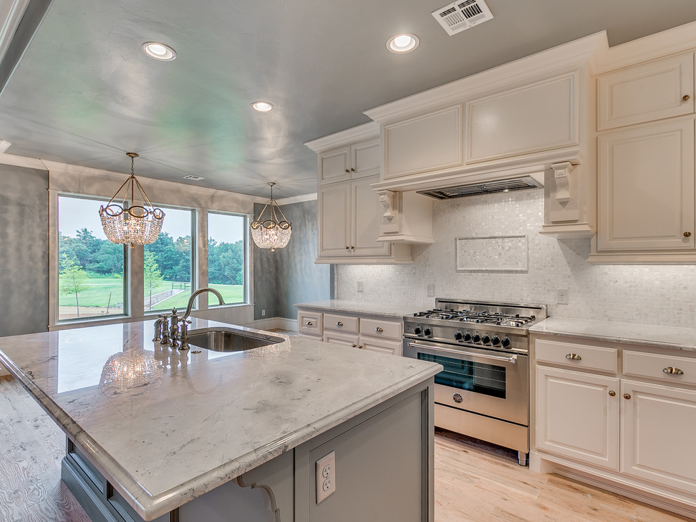Design ideas for a mid-sized transitional l-shaped eat-in kitchen in Oklahoma City with a single-bowl sink, raised-panel cabinets, white cabinets, granite benchtops, white splashback, mosaic tile splashback, stainless steel appliances, light hardwood floors and with island.