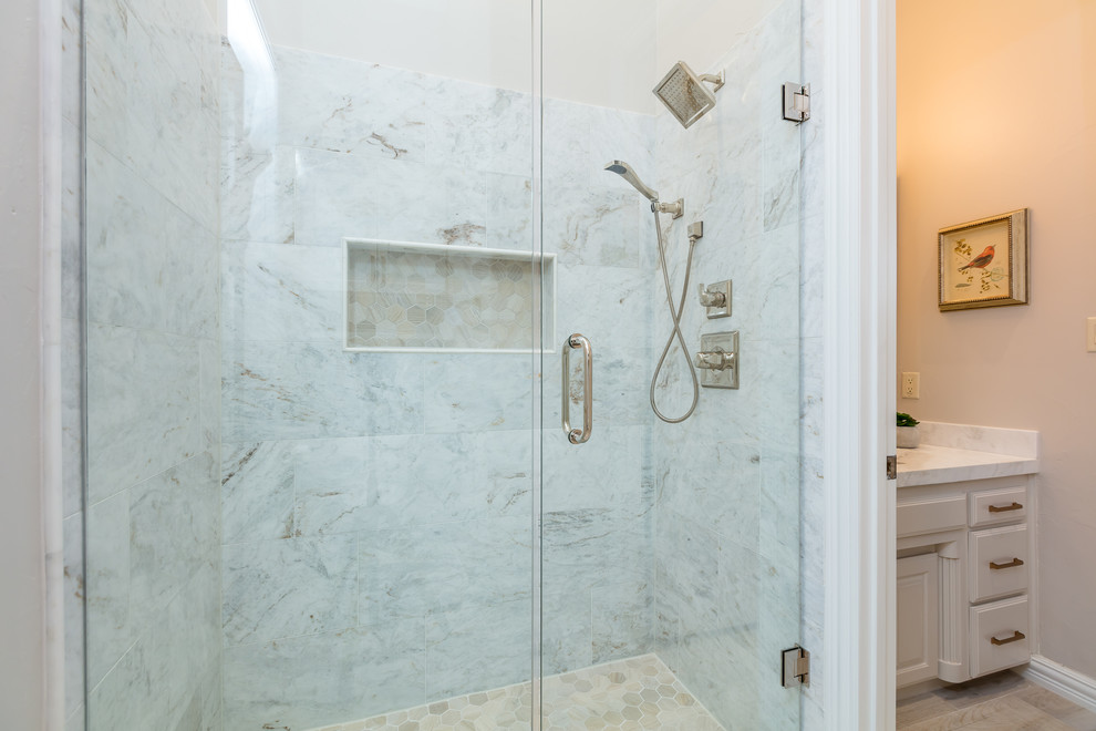 This is an example of a mid-sized transitional bathroom in Dallas with recessed-panel cabinets, beige cabinets, a two-piece toilet, white tile, marble, beige walls, porcelain floors, an undermount sink, marble benchtops, beige floor, a hinged shower door and white benchtops.