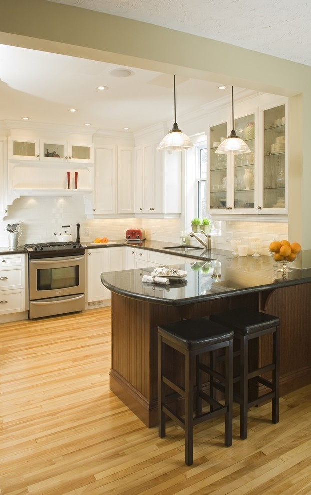 Mid-sized transitional u-shaped kitchen in Toronto with an undermount sink, shaker cabinets, white cabinets, white splashback, subway tile splashback, stainless steel appliances, medium hardwood floors, a peninsula and brown floor.