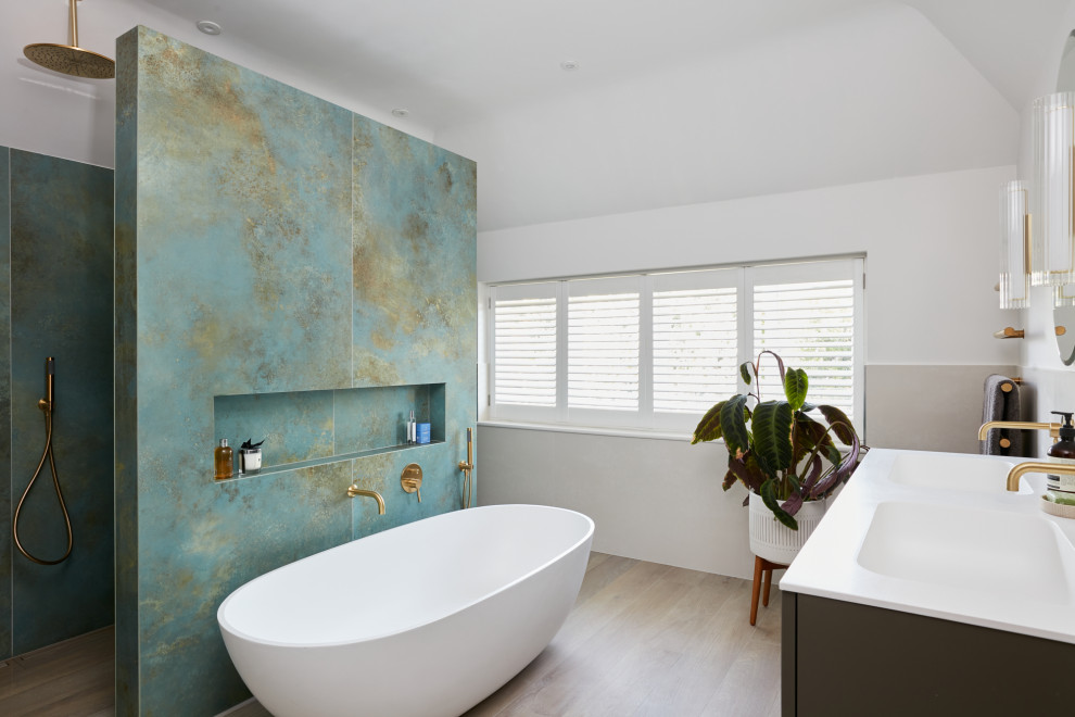 Inspiration for a large contemporary ensuite bathroom in London with a freestanding bath, green tiles, an integrated sink, a hinged door, double sinks, a floating vanity unit, grey cabinets, white walls, wood-effect flooring, engineered stone worktops, beige floors and white worktops.