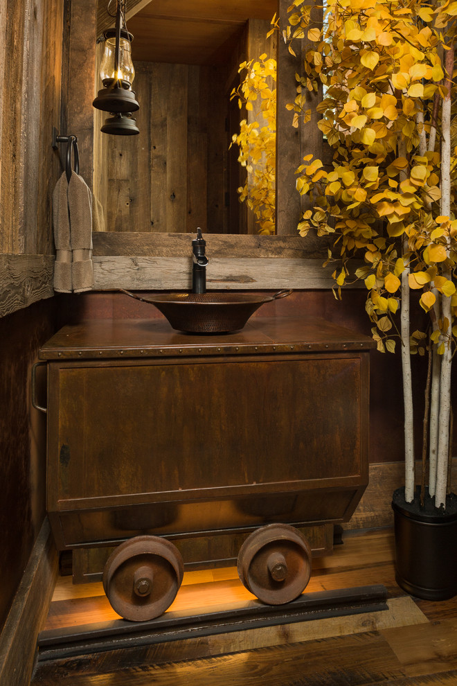 Photo of a small country powder room in Other with brown walls, a vessel sink, brown floor, brown benchtops, furniture-like cabinets, distressed cabinets and dark hardwood floors.
