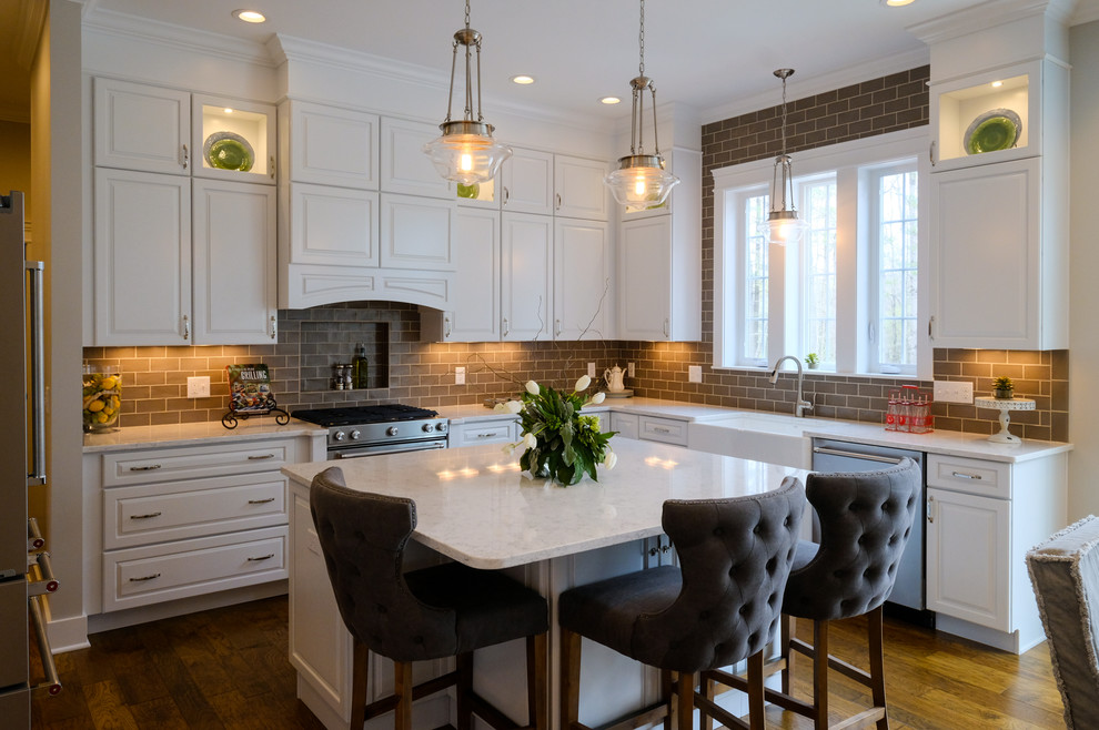 Example of a mid-sized transitional u-shaped medium tone wood floor and brown floor eat-in kitchen design with white cabinets, an island, a farmhouse sink, raised-panel cabinets, brown backsplash, stainless steel appliances and quartz countertops
