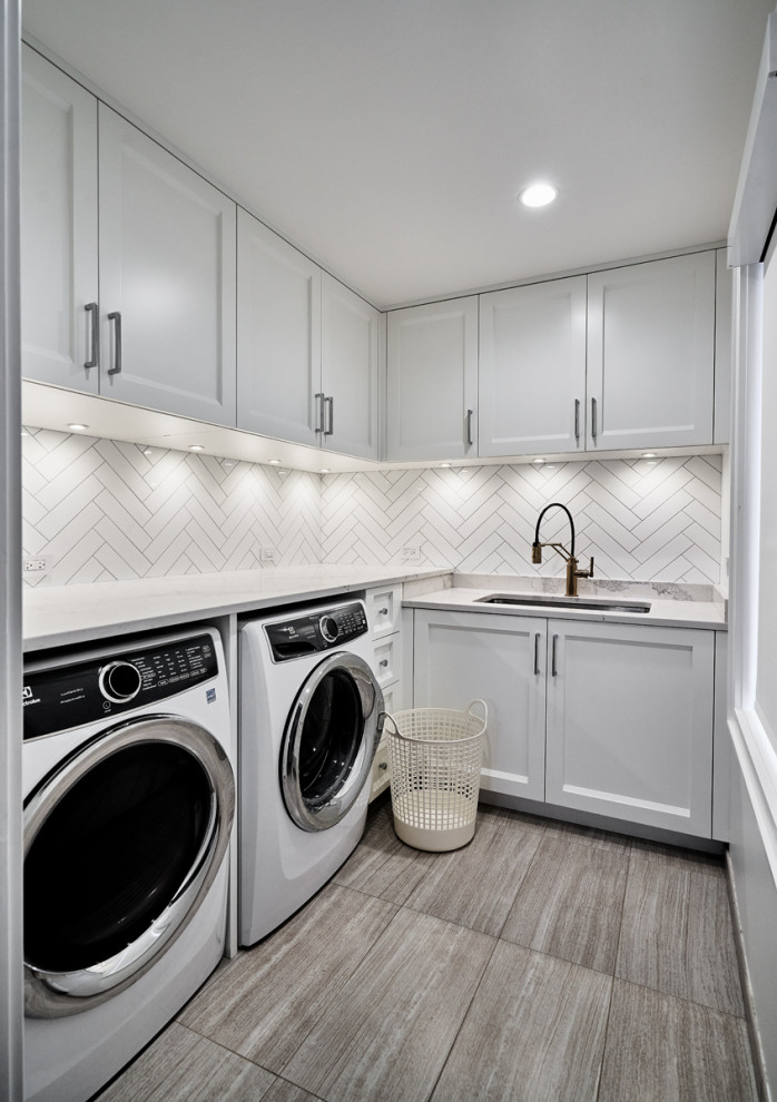 This is an example of a small modern l-shaped dedicated laundry room in Chicago with a single-bowl sink, recessed-panel cabinets, white cabinets, quartz benchtops, white splashback, subway tile splashback, white walls, porcelain floors, a side-by-side washer and dryer, beige floor and white benchtop.