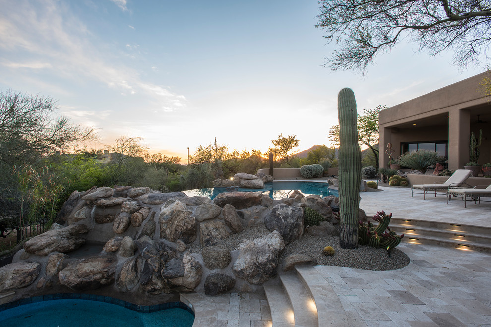 Large backyard custom-shaped infinity pool in Phoenix with natural stone pavers.