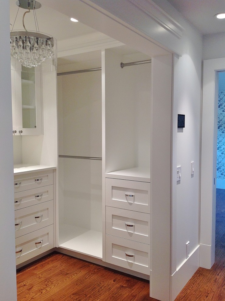 This is an example of a large traditional women's walk-in wardrobe in Calgary with white cabinets, medium hardwood floors and shaker cabinets.