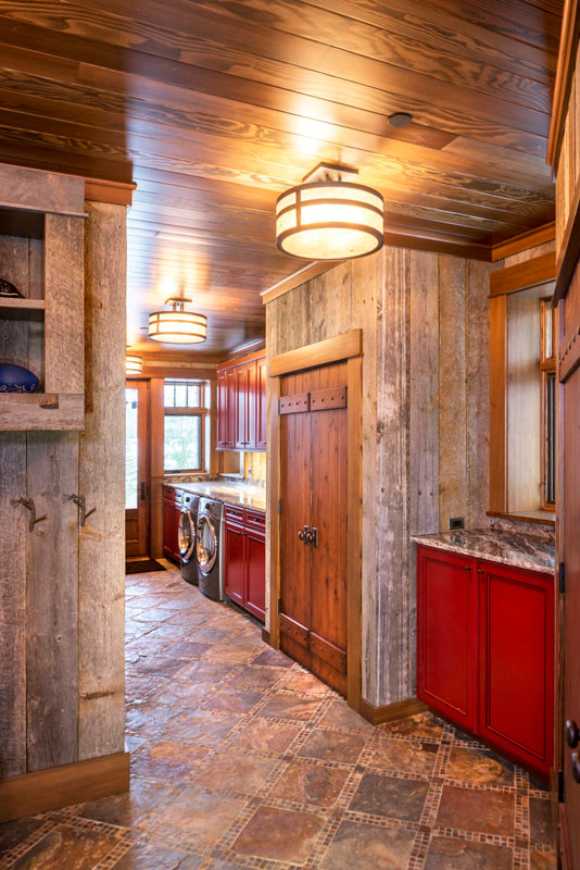 This is an example of a large country single-wall utility room in New York with recessed-panel cabinets, granite benchtops, grey walls, slate floors, a side-by-side washer and dryer, multi-coloured floor, grey benchtop and red cabinets.