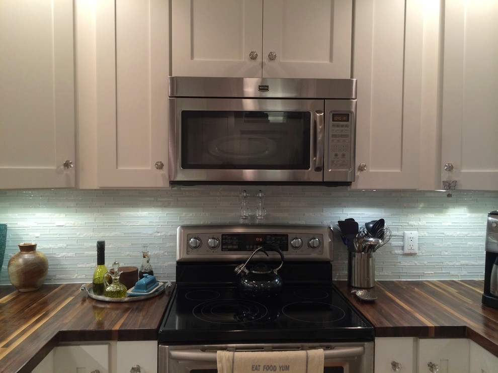 Example of a mid-sized transitional u-shaped porcelain tile and beige floor enclosed kitchen design in Miami with an undermount sink, shaker cabinets, white cabinets, wood countertops, blue backsplash, glass tile backsplash, stainless steel appliances and a peninsula