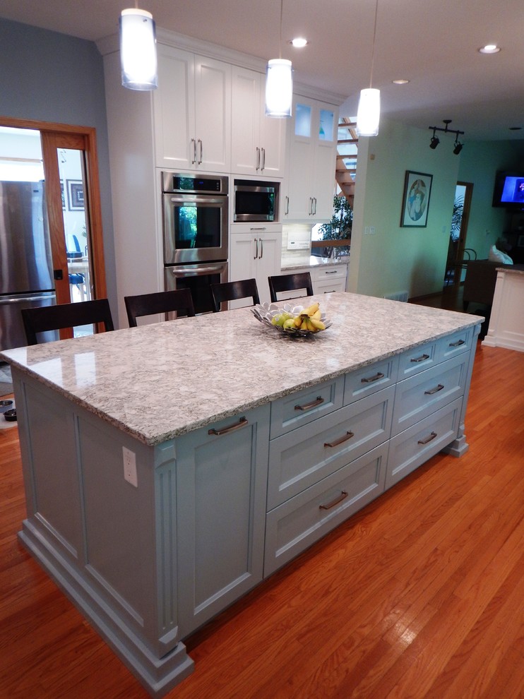 Eat-in kitchen - large transitional l-shaped light wood floor eat-in kitchen idea with an undermount sink, recessed-panel cabinets, white cabinets, quartz countertops, gray backsplash, stone tile backsplash, stainless steel appliances and an island