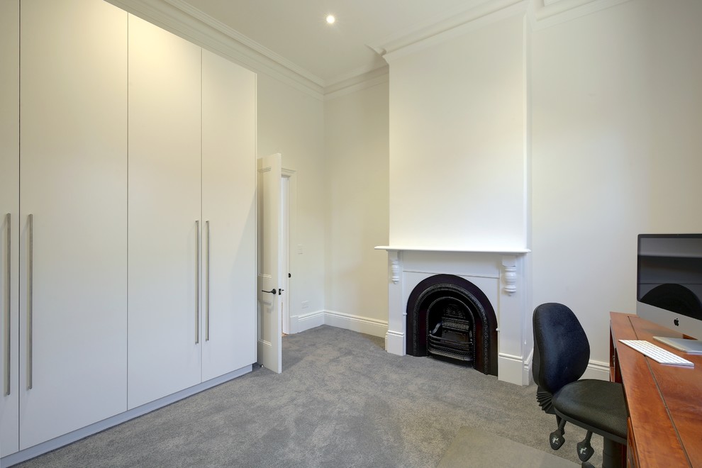 Photo of a mid-sized modern study room in Adelaide with white walls, carpet, a standard fireplace, a wood fireplace surround, a freestanding desk and grey floor.