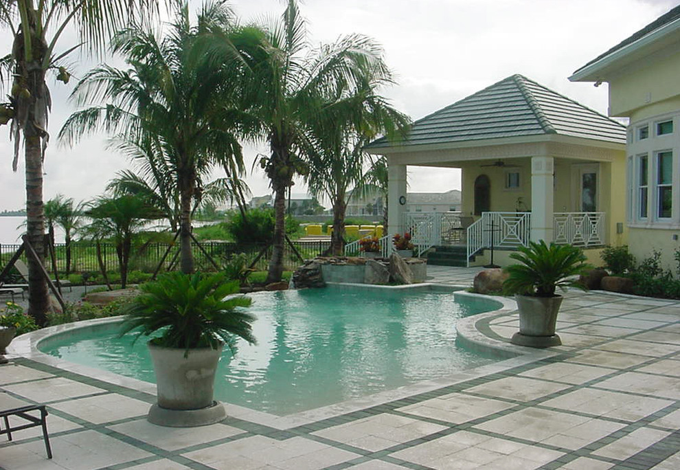 Expansive tropical backyard custom-shaped natural pool in Tampa with a water feature and natural stone pavers.