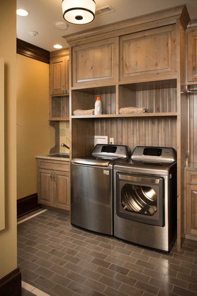 Inspiration for a mid-sized transitional single-wall dedicated laundry room in Charleston with an undermount sink, raised-panel cabinets, solid surface benchtops, yellow walls, porcelain floors, a side-by-side washer and dryer and medium wood cabinets.