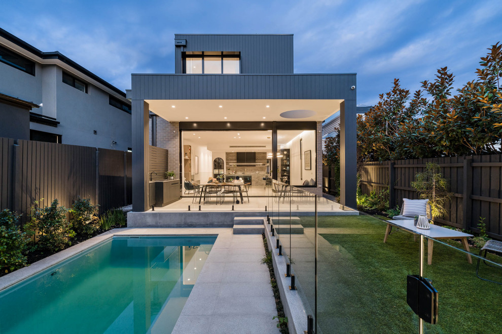 Large and black contemporary two floor detached house in Melbourne with wood cladding, a flat roof, a metal roof and board and batten cladding.