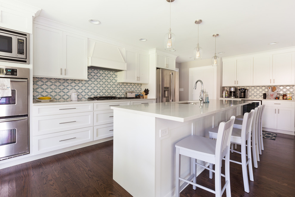 Inspiration for a large contemporary l-shaped open plan kitchen in Chicago with an undermount sink, shaker cabinets, white cabinets, quartz benchtops, white splashback, stainless steel appliances, medium hardwood floors, with island, brown floor and white benchtop.