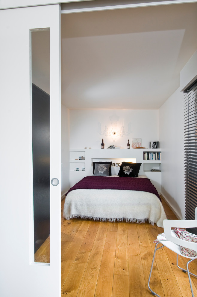 Photo of a contemporary bedroom in Paris with white walls and medium hardwood floors.