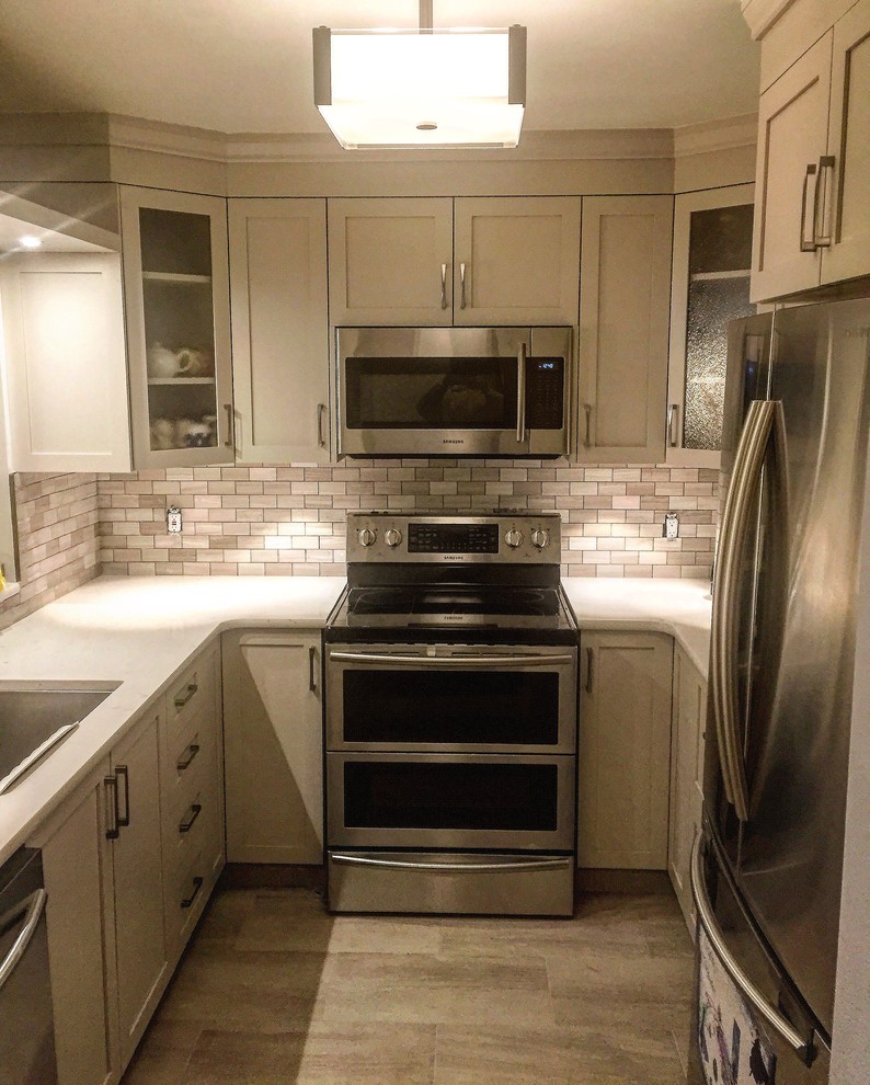 Kitchen - small transitional u-shaped porcelain tile and brown floor kitchen idea in Toronto with an undermount sink, shaker cabinets, beige cabinets, gray backsplash, subway tile backsplash and stainless steel appliances