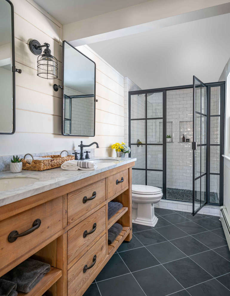 Photo of a mid-sized transitional master bathroom in Boston with medium wood cabinets, white tile, subway tile, white walls, slate floors, an undermount sink, marble benchtops, grey floor, a hinged shower door, white benchtops, a double vanity, a built-in vanity, planked wall panelling and a niche.