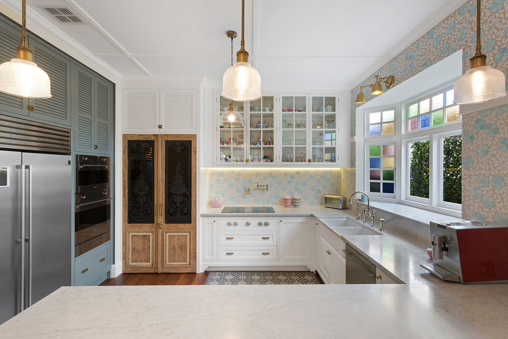 Photo of a transitional u-shaped kitchen in Melbourne with a farmhouse sink, louvered cabinets, white cabinets, multi-coloured splashback, mosaic tile splashback, stainless steel appliances, dark hardwood floors, a peninsula, brown floor and grey benchtop.