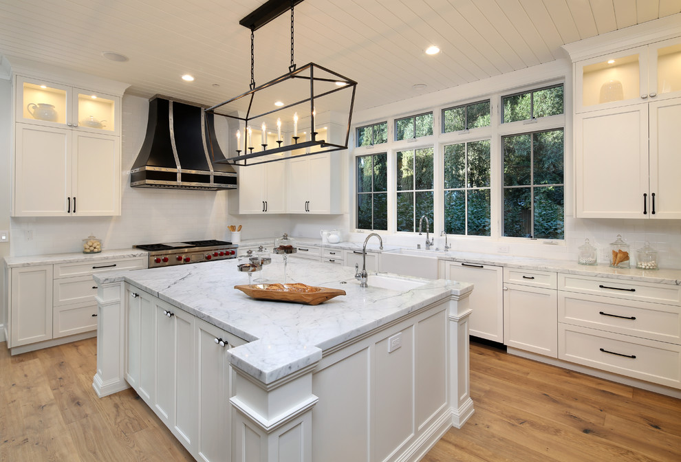 Inspiration for a traditional l-shaped kitchen in San Francisco with a farmhouse sink, shaker cabinets, white cabinets, white splashback, subway tile splashback, panelled appliances, medium hardwood floors and with island.