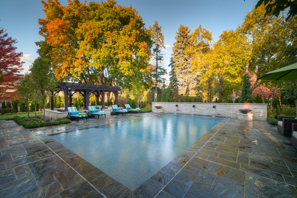 This is an example of a large traditional backyard rectangular pool in Toronto with a water feature and natural stone pavers.