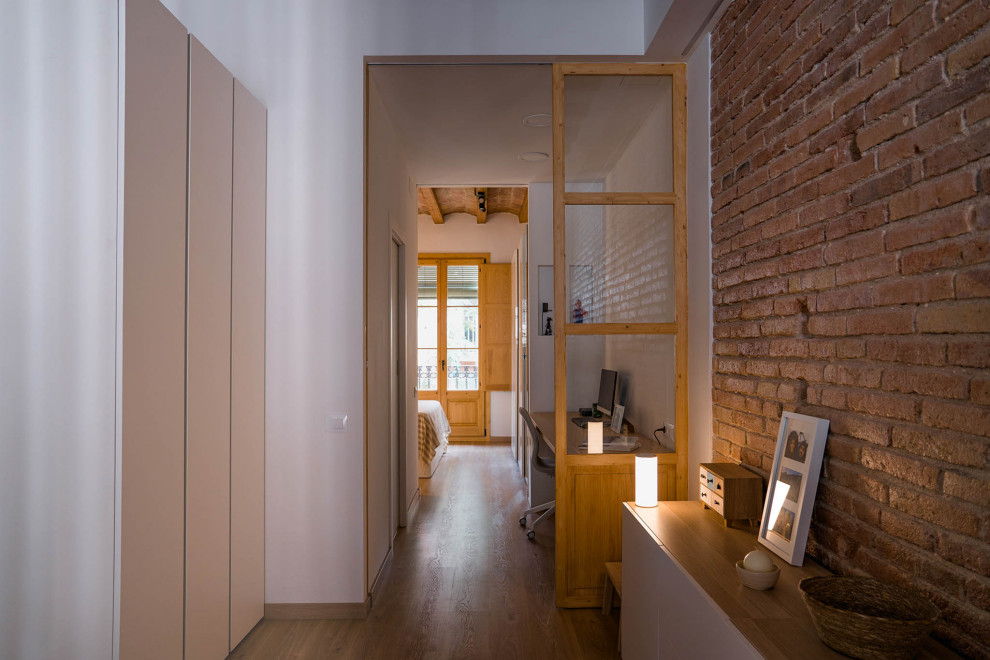 Example of a mid-sized mountain style medium tone wood floor, brown floor, exposed beam and brick wall hallway design in Barcelona with white walls