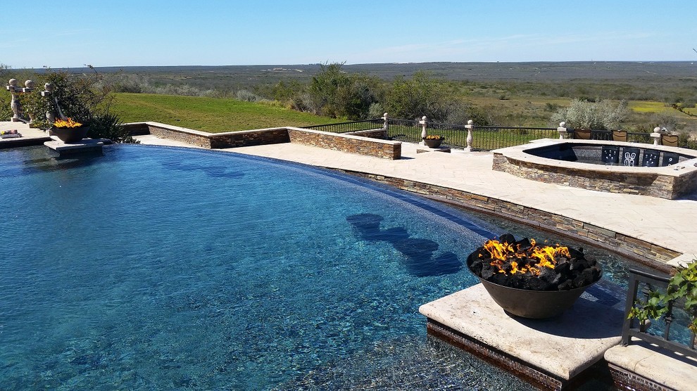 Inspiration for a large traditional backyard custom-shaped infinity pool in Houston with a hot tub and natural stone pavers.