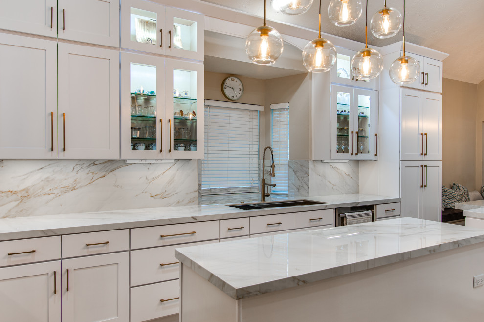 Photo of a large modern l-shaped eat-in kitchen in Houston with an undermount sink, shaker cabinets, white cabinets, solid surface benchtops, white splashback, porcelain splashback, stainless steel appliances, marble floors, with island, beige floor and white benchtop.