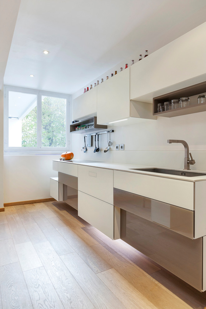 Photo of a large contemporary l-shaped eat-in kitchen in Paris with an undermount sink, glass-front cabinets, white cabinets, quartzite benchtops, white splashback, glass tile splashback, stainless steel appliances, light hardwood floors and multiple islands.
