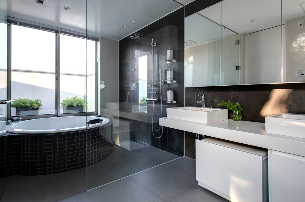Photo of a mid-sized contemporary master bathroom in Yokohama with a drop-in tub, an open shower, black tile, a vessel sink, white cabinets, flat-panel cabinets, black walls, slate floors and an open shower.