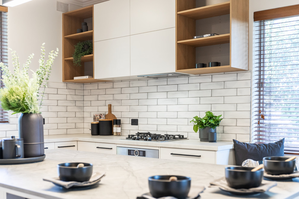This is an example of a large contemporary u-shaped eat-in kitchen in Adelaide with a double-bowl sink, flat-panel cabinets, white cabinets, quartz benchtops, white splashback, subway tile splashback, black appliances, light hardwood floors, with island, yellow floor and grey benchtop.
