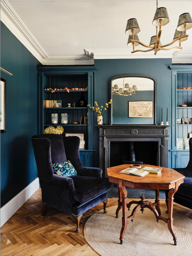 Photo of a large traditional enclosed family room in London with a game room, blue walls, medium hardwood floors, a wood stove, a metal fireplace surround and brown floor.