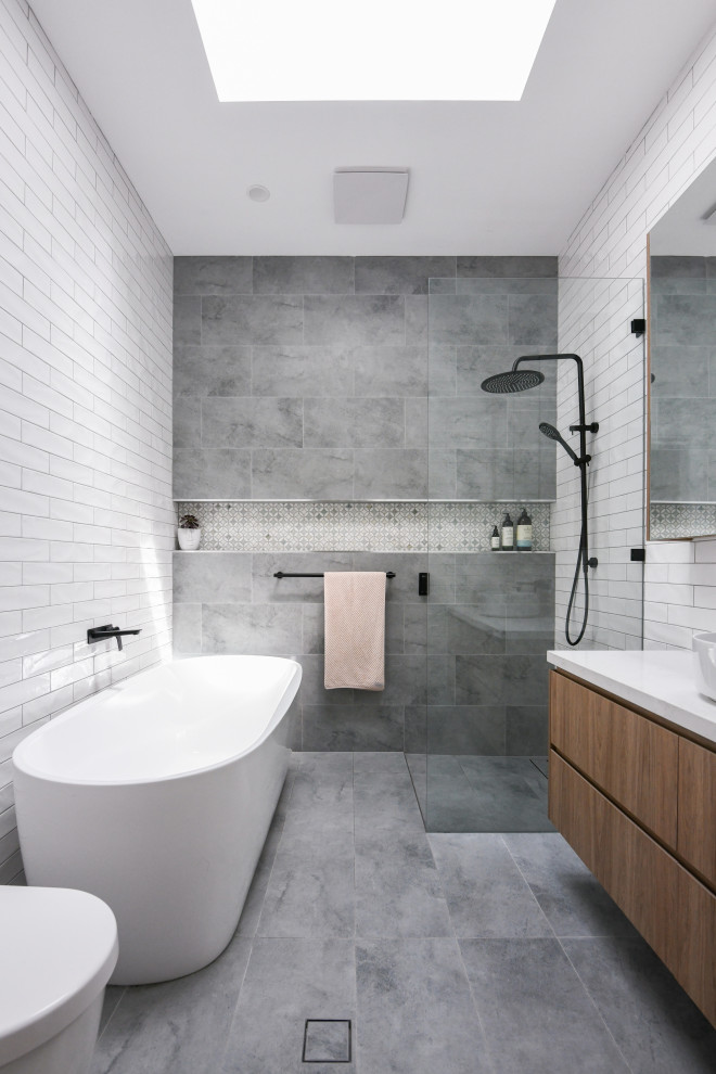 Photo of a large scandinavian master bathroom in Sydney with flat-panel cabinets, medium wood cabinets, a freestanding tub, an open shower, a one-piece toilet, white tile, ceramic tile, white walls, ceramic floors, a drop-in sink, engineered quartz benchtops, grey floor, an open shower, white benchtops, a niche, a single vanity and a floating vanity.