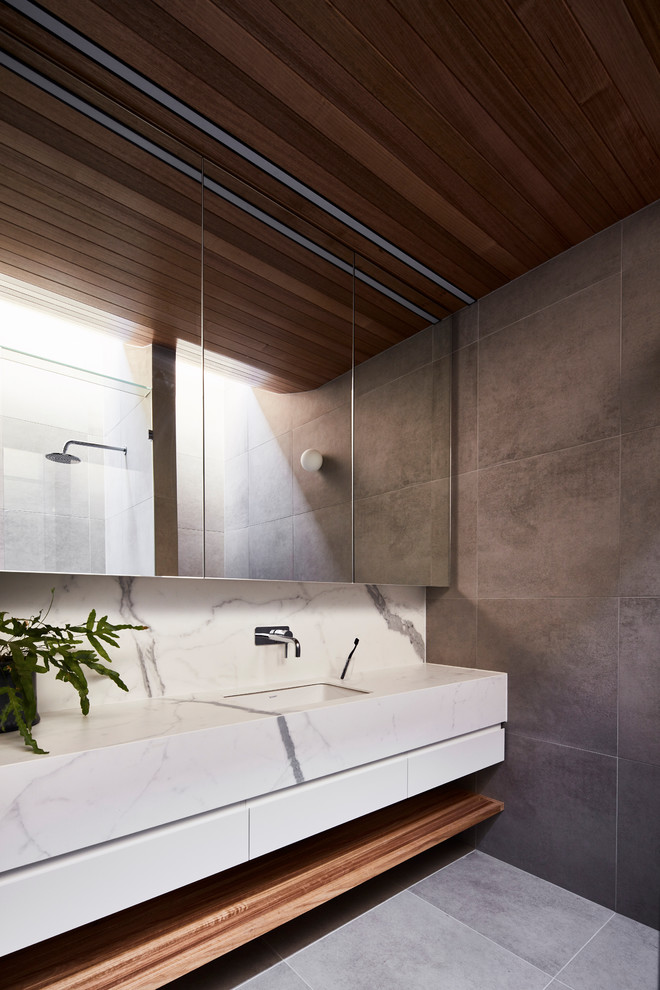 Inspiration for a contemporary master bathroom in Melbourne with flat-panel cabinets, white cabinets, a double shower, a wall-mount toilet, gray tile, porcelain tile, grey walls, porcelain floors, an undermount sink, marble benchtops, grey floor, a hinged shower door and white benchtops.