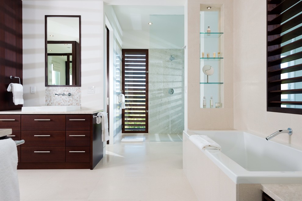 This is an example of a mid-sized tropical kids bathroom in London with furniture-like cabinets, dark wood cabinets, a drop-in tub, an open shower, a wall-mount toilet, white tile, ceramic tile, beige walls and limestone floors.