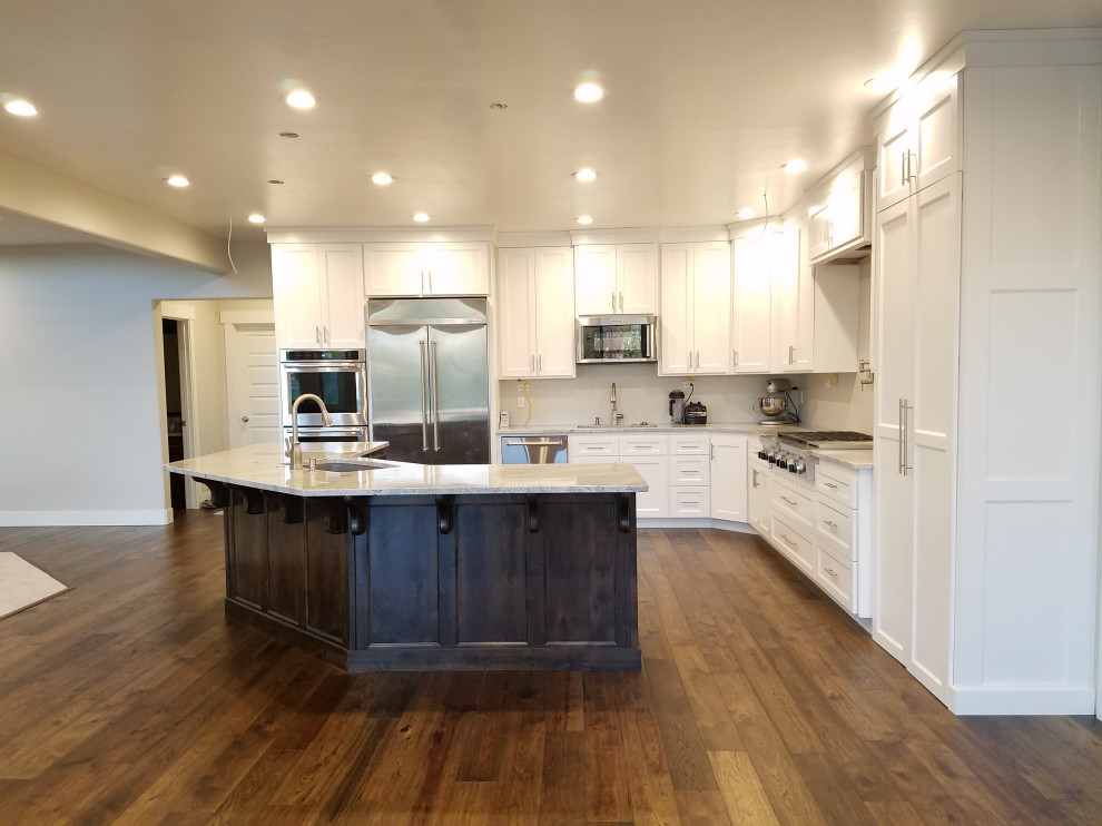 This is an example of a large country l-shaped eat-in kitchen in Los Angeles with an undermount sink, recessed-panel cabinets, white cabinets, granite benchtops, white splashback, shiplap splashback, stainless steel appliances, medium hardwood floors, with island, multi-coloured floor, multi-coloured benchtop and vaulted.