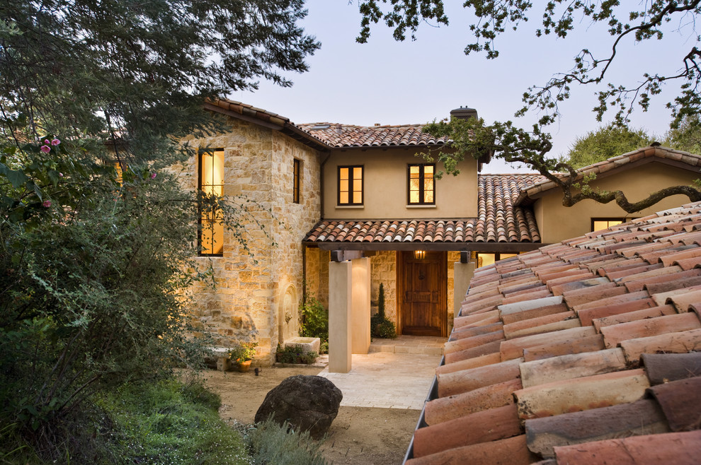 Photo of a mediterranean two-storey exterior in San Francisco with stone veneer and a tile roof.
