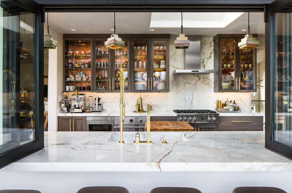 Photo of a large eclectic u-shaped eat-in kitchen in San Francisco with a drop-in sink, glass-front cabinets, grey cabinets, marble benchtops, white splashback, stone slab splashback, stainless steel appliances, terra-cotta floors and with island.