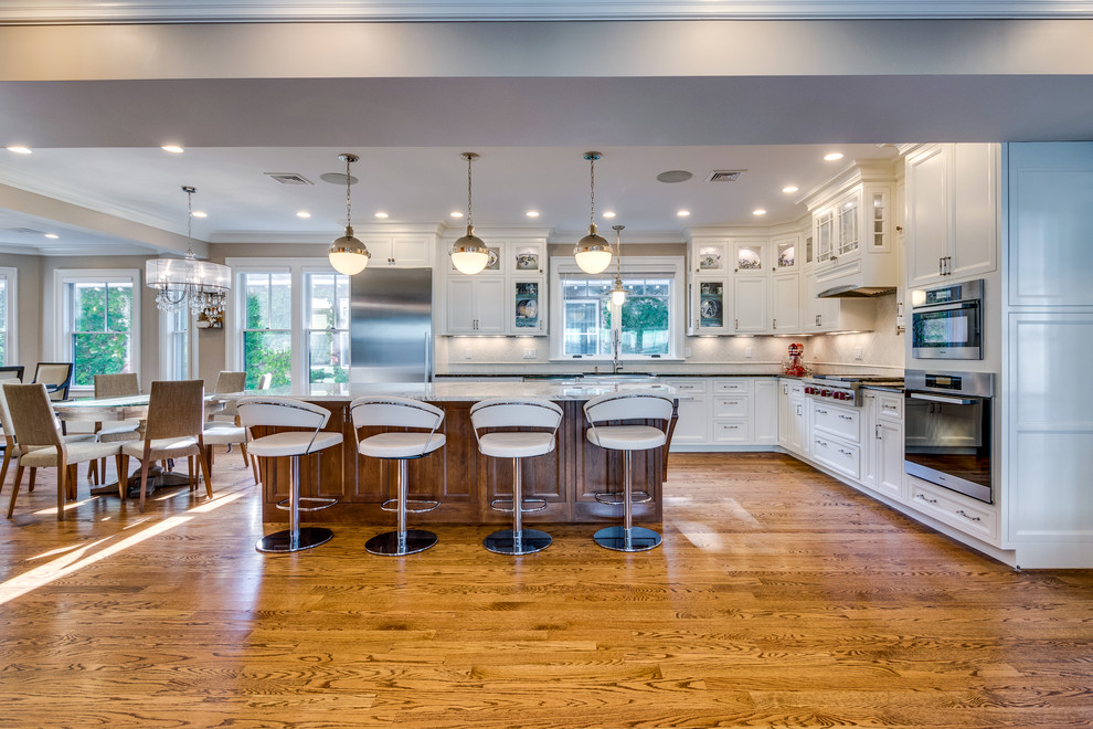 Inspiration for a mid-sized transitional l-shaped medium tone wood floor and brown floor open concept kitchen remodel in Boston with a farmhouse sink, recessed-panel cabinets, white cabinets, soapstone countertops, beige backsplash, ceramic backsplash, stainless steel appliances and an island