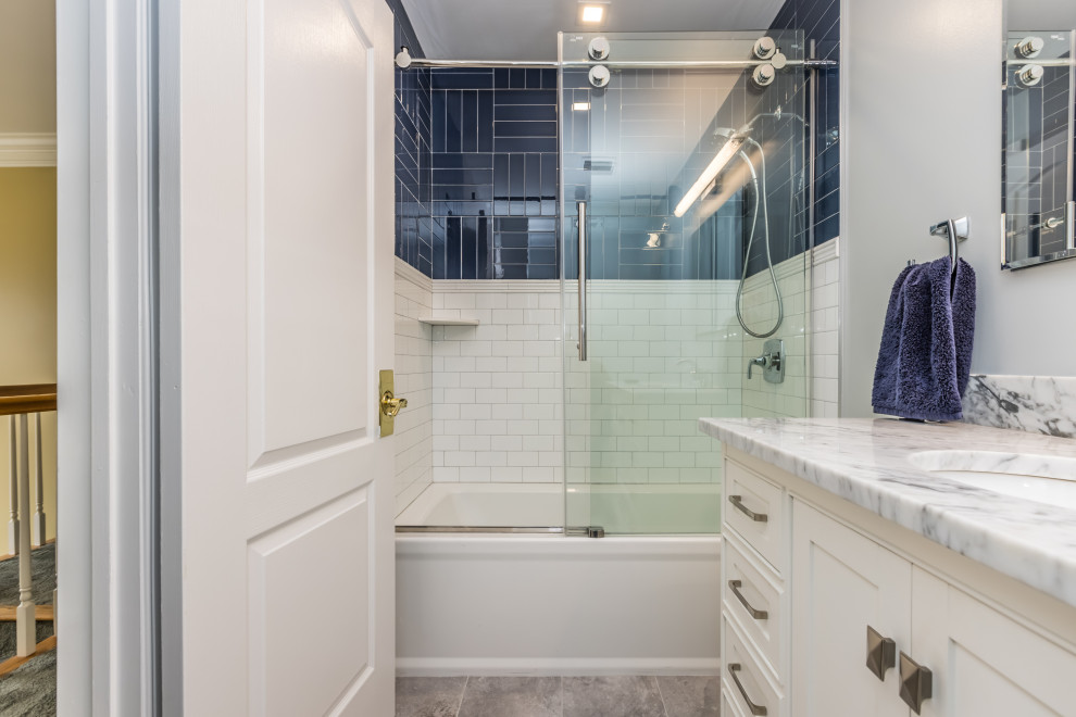 На фото: детская ванная комната среднего размера в стиле неоклассика (современная классика) с фасадами в стиле шейкер, белыми фасадами, ванной в нише, душем над ванной, раздельным унитазом, синей плиткой, стеклянной плиткой, синими стенами, полом из керамогранита, врезной раковиной, мраморной столешницей, серым полом, душем с раздвижными дверями, серой столешницей, тумбой под одну раковину и напольной тумбой