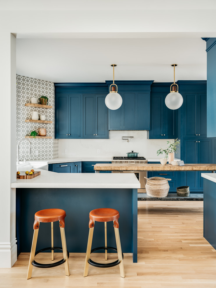 Inspiration for a transitional u-shaped kitchen in San Francisco with a farmhouse sink, shaker cabinets, blue cabinets, white splashback, light hardwood floors, with island, beige floor and white benchtop.