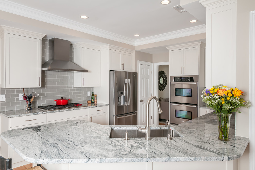 This is an example of a transitional u-shaped kitchen in Atlanta with an undermount sink, shaker cabinets, white cabinets, grey splashback, stainless steel appliances, light hardwood floors and no island.