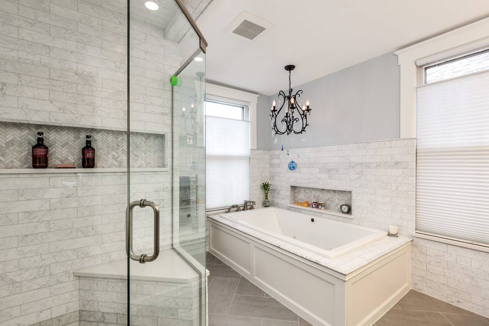 This is an example of a large transitional master bathroom in Detroit with a drop-in tub, a corner shower, gray tile, white tile, marble, porcelain floors, brown floor, a hinged shower door and grey walls.