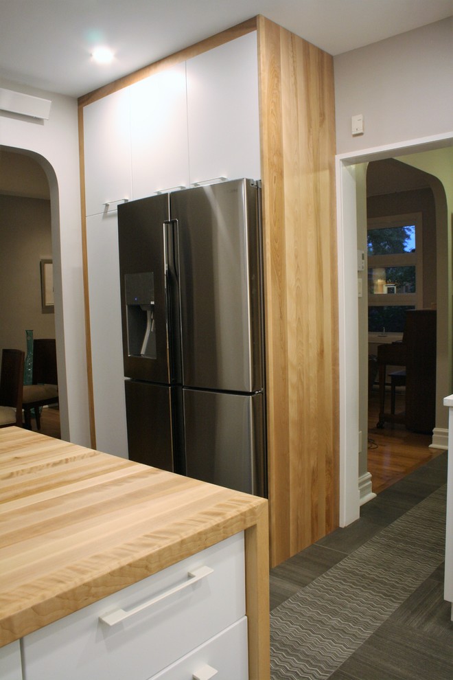 Photo of a mid-sized contemporary l-shaped kitchen pantry in Montreal with an undermount sink, flat-panel cabinets, white cabinets, wood benchtops, grey splashback, ceramic splashback, stainless steel appliances, porcelain floors, with island and grey floor.