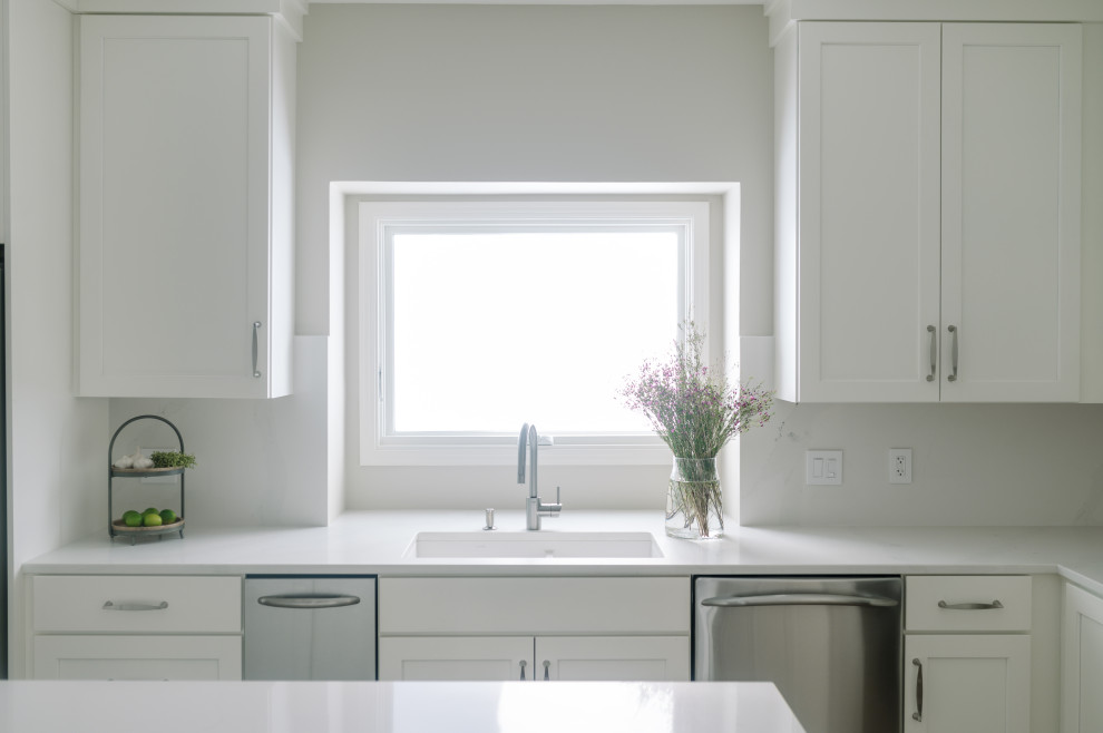 Large transitional l-shaped laminate floor and brown floor eat-in kitchen photo with an undermount sink, shaker cabinets, white cabinets, quartz countertops, white backsplash, quartz backsplash, stainless steel appliances, an island and white countertops