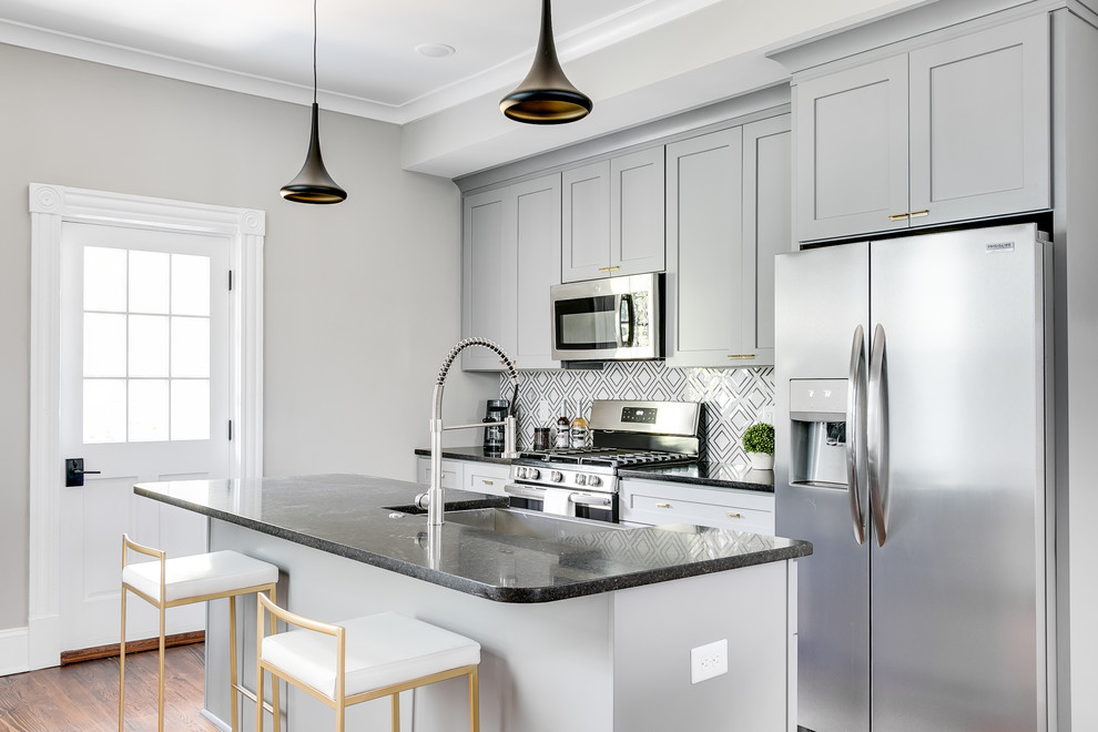 Example of a transitional medium tone wood floor kitchen design in Richmond with a farmhouse sink, shaker cabinets, gray cabinets, multicolored backsplash, stainless steel appliances, an island and black countertops