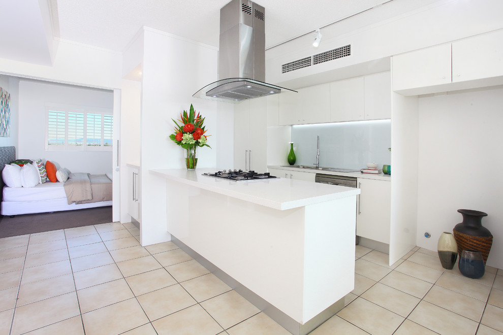 Inspiration for a mid-sized beach style galley open plan kitchen in Gold Coast - Tweed with a drop-in sink, flat-panel cabinets, white cabinets, quartz benchtops, white splashback, glass sheet splashback, stainless steel appliances, ceramic floors and with island.