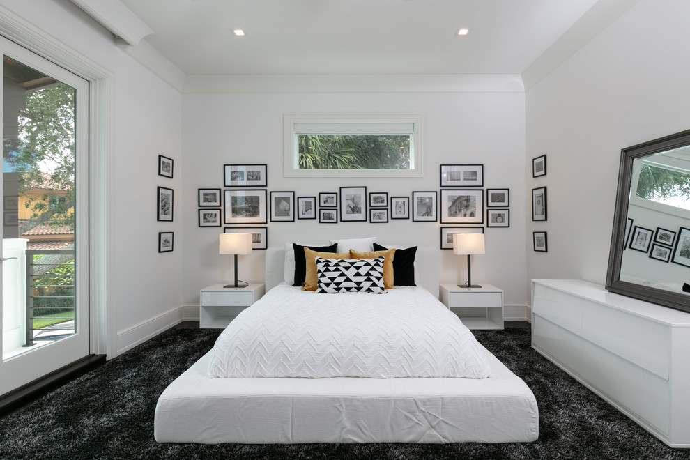 This is an example of a beach style bedroom in Tampa with white walls, carpet, no fireplace and black floor.