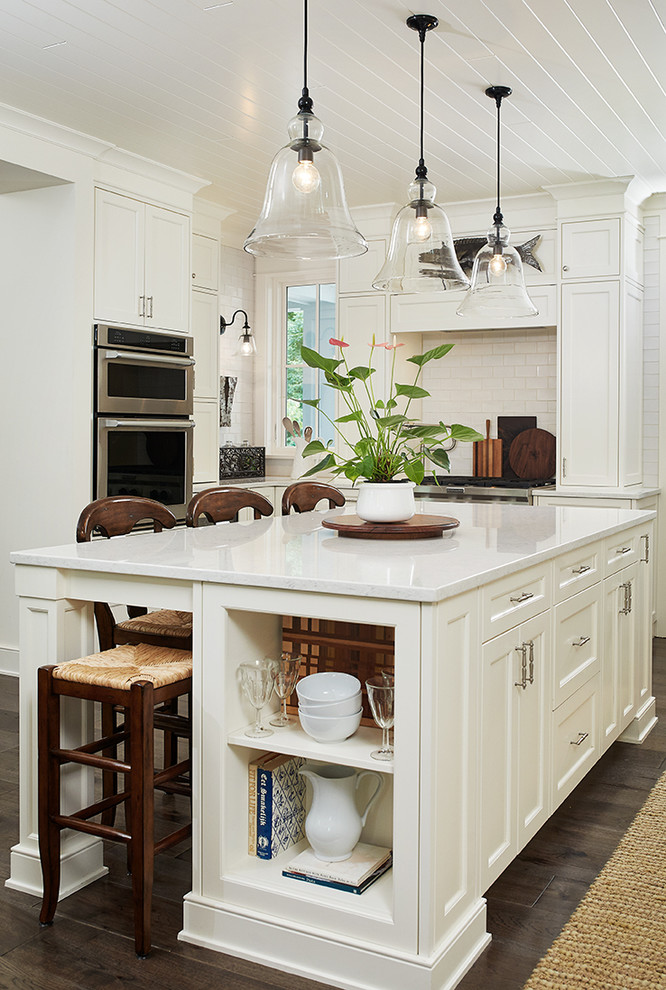 Design ideas for a transitional u-shaped kitchen in Grand Rapids with a farmhouse sink, white cabinets, dark hardwood floors, with island, brown floor, white splashback, subway tile splashback, stainless steel appliances and recessed-panel cabinets.