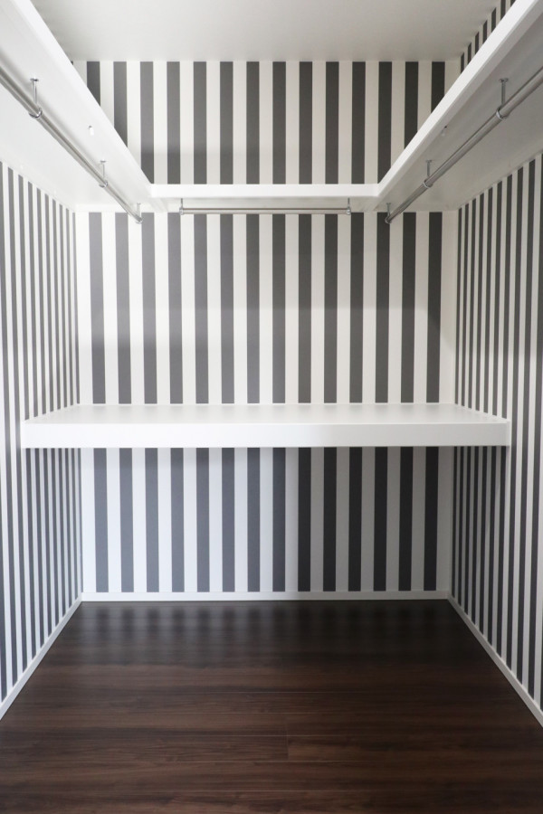 Diseño de armario vestidor unisex con suelo de madera oscura y papel pintado